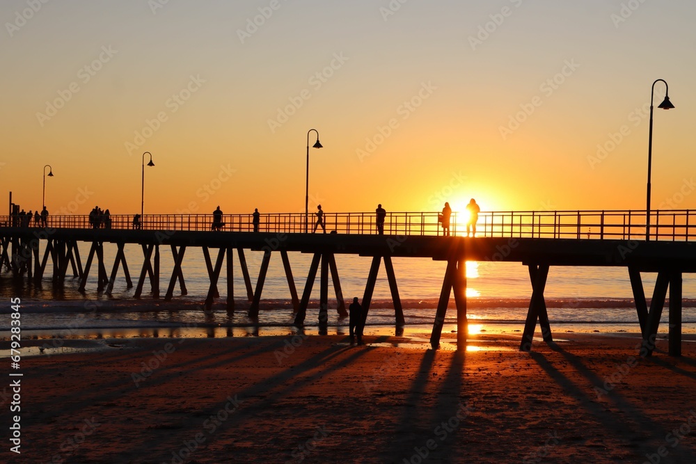 Group of people enjoying a stroll along a boardwalk at sunset in Glenelg Beach, Adelaide, Australia