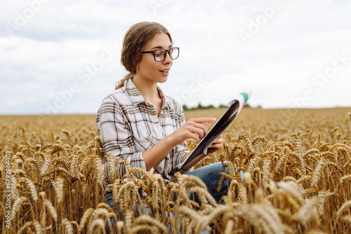 Young female farmer checking crop growth with clipboard in golden wheat field. Smart farming. Agribusiness.