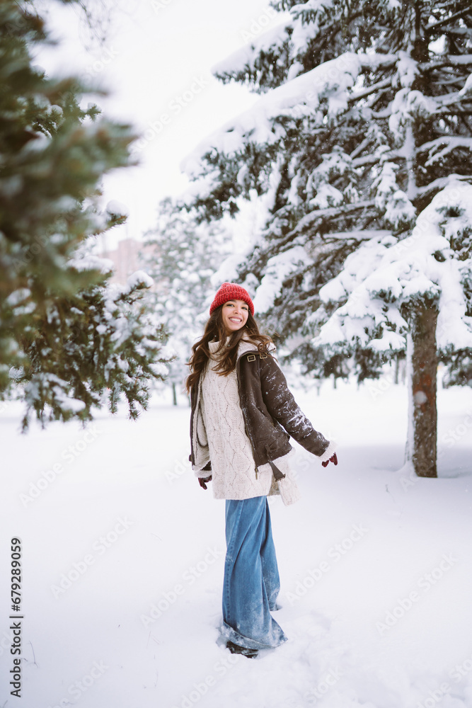 Portrait of a young happy woman having fun in a snowy park. Happy woman in a red hat and scarf walking outdoors. Portrait of a young happy woman having fun in a snowy park. Happy woman in a red hat and scarf walking outdoors.