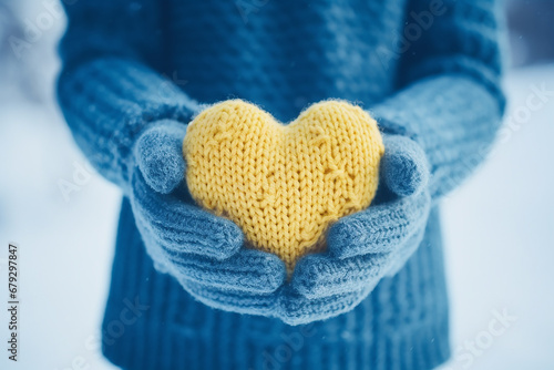 Fragment. The hands of a girl in a blue sweater holds a knitted heart against the background of falling snow