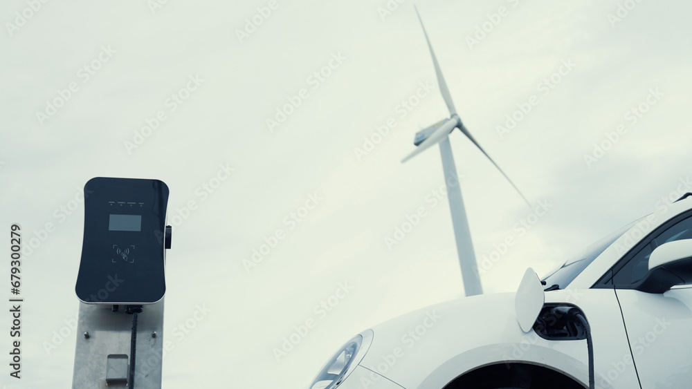 © InfiniteFlow - Progressive future energy infrastructure concept of electric vehicle being charged at charging station powered by green and renewable energy from a wind turbine in order to preserve the environment. © InfiniteFlow - Progressive future energy infrastructure concept of electric vehicle being charged at charging station powered by green and renewable energy from a wind turbine in order to preserve the environment.