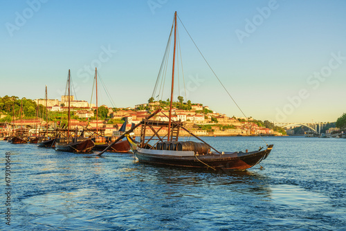 Traditional Portuguese wooden cargo boats rabelo on the Douro River with Porto city on background at sunrise, Portugal. Travel destination photo