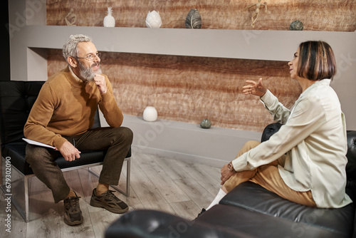 bearded middle aged psychologist in glasses talking to female client during therapy session
