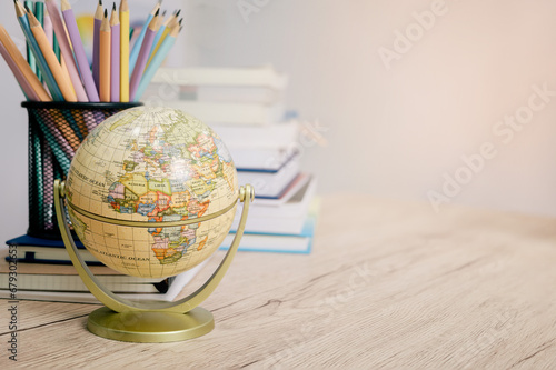 Education concept featuring globes, colorful pencils, pens, and books on a modern table against a bright background
