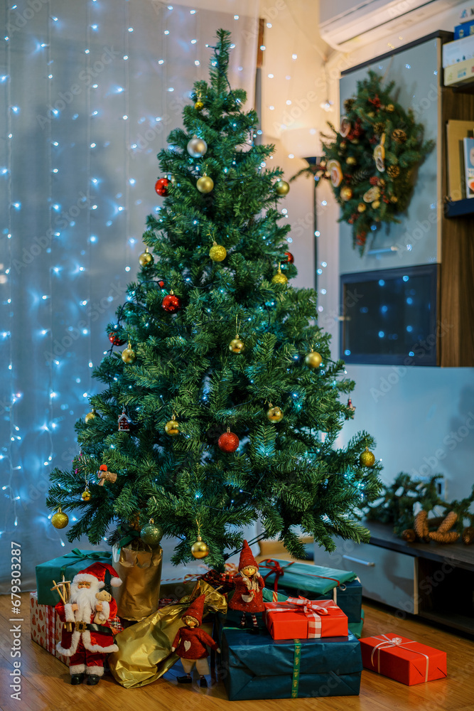 Colorful gifts lie under the Christmas tree next to the figurines of Santa Claus and elves