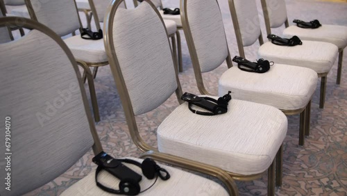 Simultaneous translation headsets lie on chairs in the conference room before the start of a press conference. Equipment for simultaneous translation at a meeting.