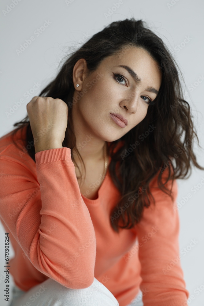 Beautiful woman of 30 years old sitting on chair, white background. Portrait of brunette girl smile. Orange sweater and light jeans. Woman barefeet, thoughtful. Beautiful woman of 30 years old sitting on chair, white background. Portrait of brunette girl smile. Orange sweater and light jeans. Woman barefeet, thoughtful.