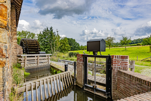 Closed water canal gate at old Eper or Wingbergermolen water mill, next Geul river, plain with trees against cloud covered sky in background, sunny day in Terpoorten, Epen, South Limburg, Netherlands photo