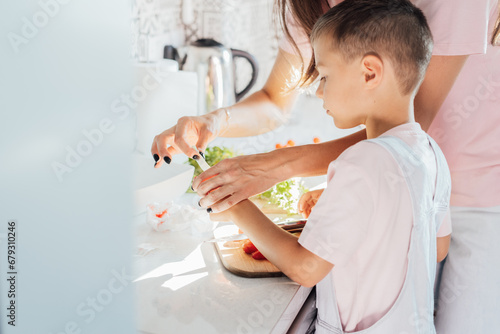Caring young Mother putting a plaster on child finger with wound on from a cut by kitchen knife. First aid in case of small domestic injury. Children's injuries at home. Negligence in cooking at home photo