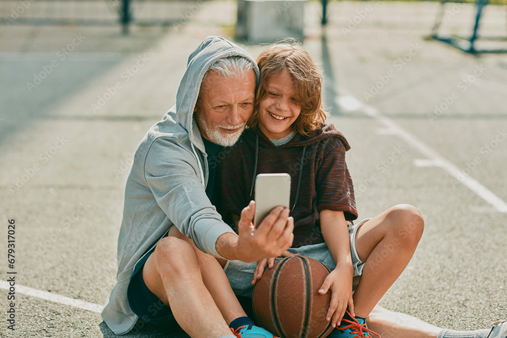© Marko Geber - Grandfather and grandson taking a selfie on a smart phone while resting from playing basketball outdoors on a basketball court in the city © Marko Geber - Grandfather and grandson taking a selfie on a smart phone while resting from playing basketball outdoors on a basketball court in the city