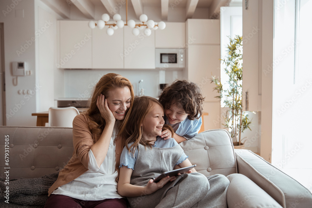 Mother and Children Sharing a Laugh While Looking at a Tablet at Home Mother and Children Sharing a Laugh While Looking at a Tablet at Home