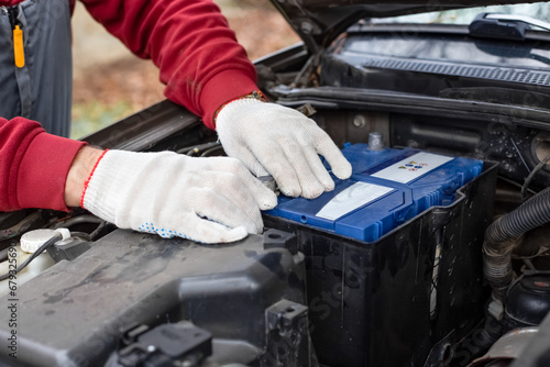 auto mechanic installs a car battery under the hood of a car. Car maintenance and repair. photo