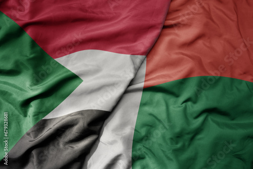 big waving national colorful flag of sudan and national flag of madagascar .