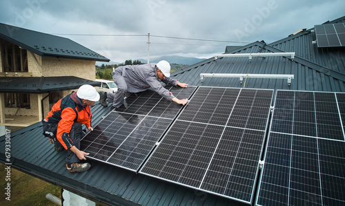 Workers installing photovoltaic solar panels on roof of house. Men engineers in helmets building solar module system with help of hex key. Concept of alternative, renewable energy.