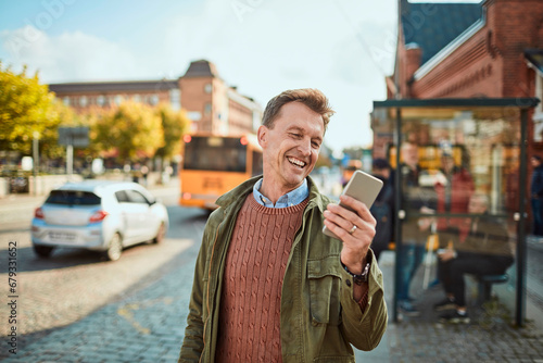 Smiling Man Texting on Smartphone at Bus Stop