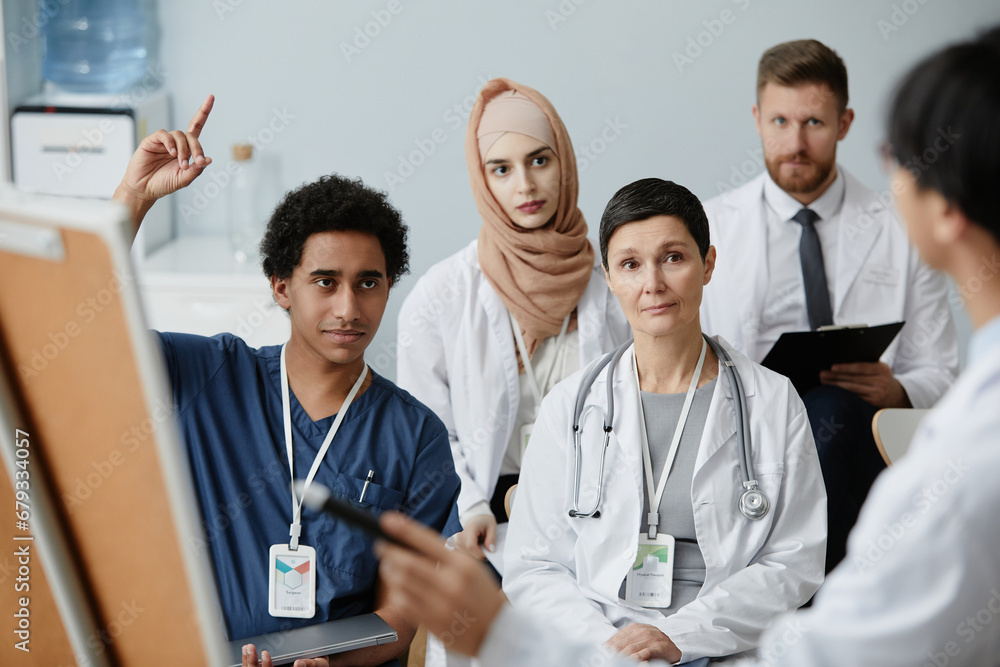 Portrait of young Middle Eastern man raising hand in audience at medical seminar Portrait of young Middle Eastern man raising hand in audience at medical seminar