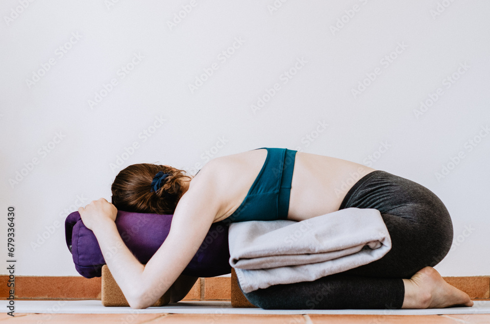 Woman doing restorative yoga child's pose with props - obrazy, fototapety, plakaty 