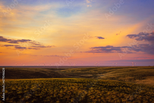 A sunset over a prairie with wind turbines in the distance.
