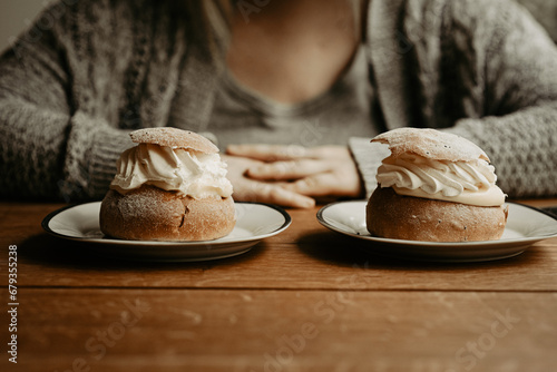 Concept of picking pastry to eat. Focus on traditional Swedish pastry, semla, on the plates at wooden table. In the background, out of focus, a person with hands on table. Photo taken in Sweden.