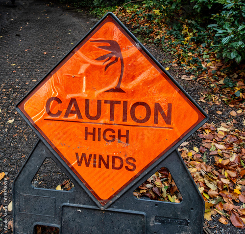  A weathered orange cautionary sign warning of high winds against a backdrop of fallen autumn leaves... photo