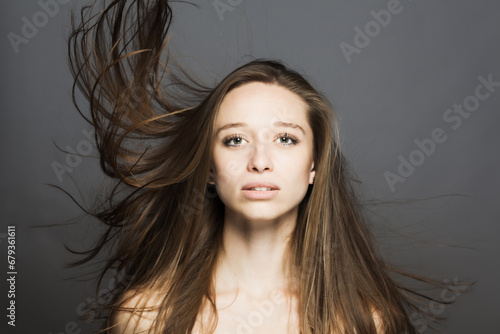 brunette girl with flowing hair in the air studio portrait against gray background...
