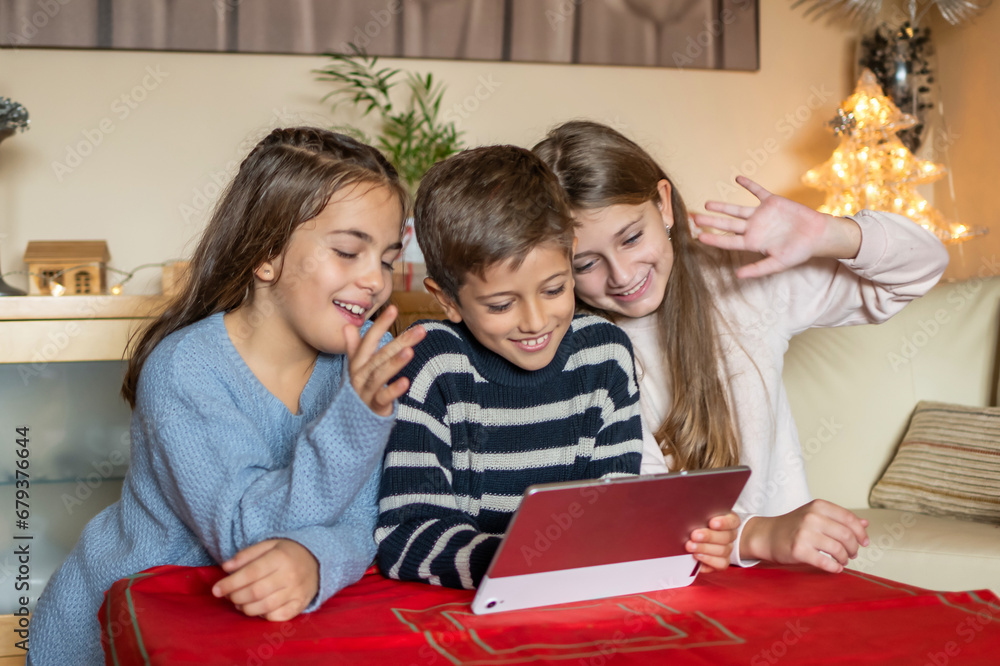 At home, three youngsters joyfully participate in a family video call, their delighted expressions evident as they share the virtual moment through a tablet. At home, three youngsters joyfully participate in a family video call, their delighted expressions evident as they share the virtual moment through a tablet.