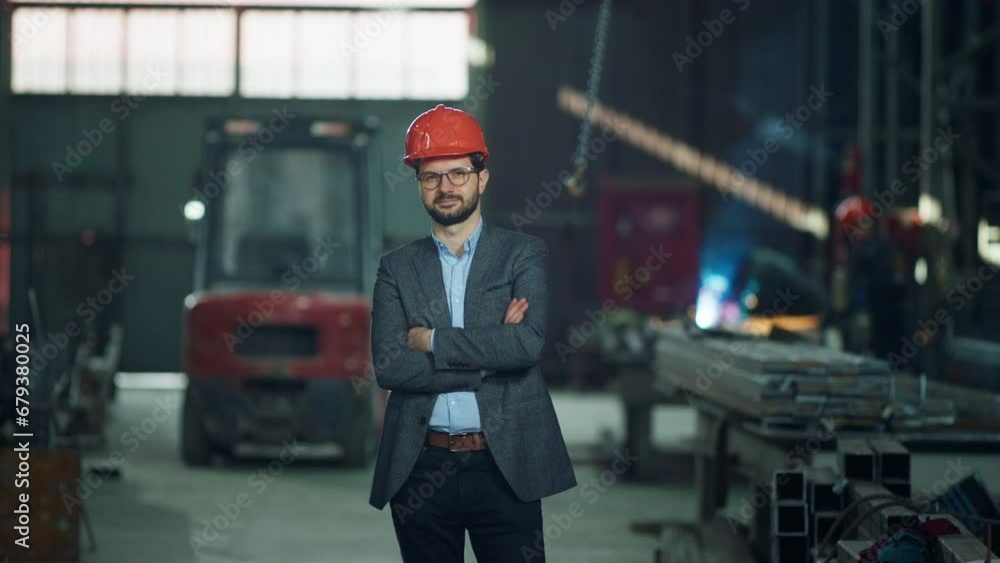 Good looking engineer in the industrial factory posing in front of the camera crossing hands and looking straight he wearing safety helmet Good looking engineer in the industrial factory posing in front of the camera crossing hands and looking straight he wearing safety helmet