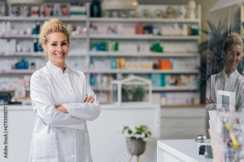 Portrait of a confident and friendly drug store assistant standing in a pharmacy with arms crossed and smiling at the camera.