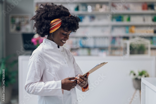 A cheerful young pharmacy worker is smiling at the clipboard while standing at her workplace. photo