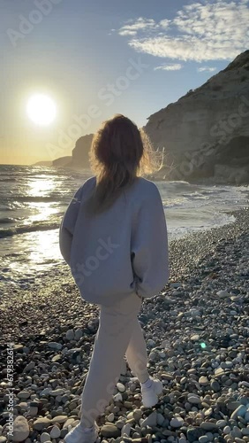 Rear view of woman in sporty clothes walking along the pebble beach