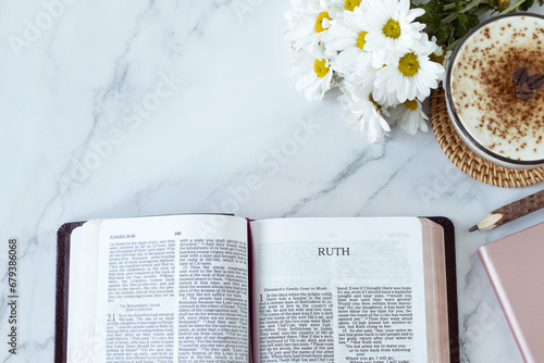 Ruth open bible book with coffee cup, flowers, pencil, and notebook on white marble background. Top table view. Copy space. Studying Old Testament Scriptures, faithful Christian woman concept.