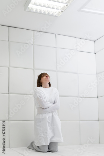 Young frustrated girl in a straitjacket is in an isolated white room in a mental hospital