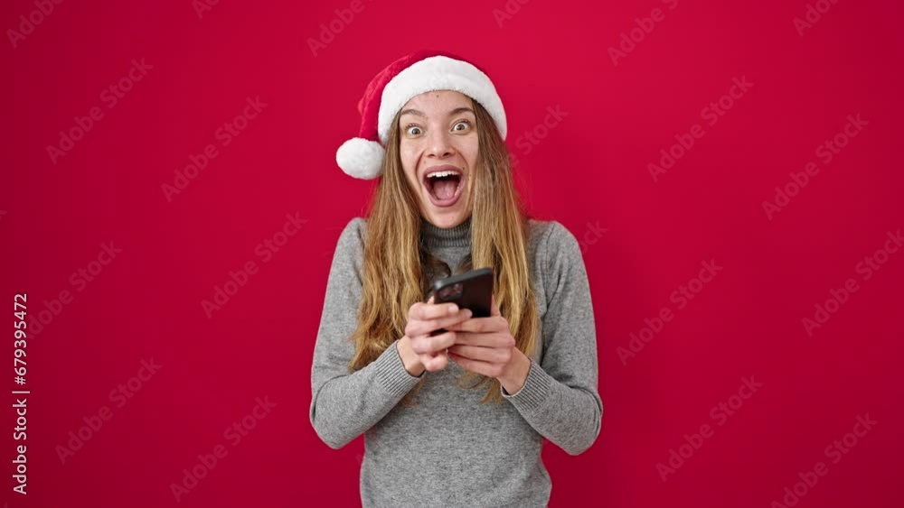 Young caucasian woman wearing christmas hat using smartphone doing ok gesture over isolated red background Young caucasian woman wearing christmas hat using smartphone doing ok gesture over isolated red background