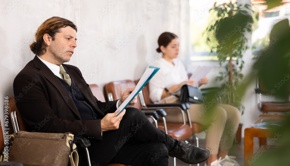 Obraz premium Unemployed man of middle age is waiting for job interview in hall. Bored male candidate for job is waiting for invitation to recruiter s office