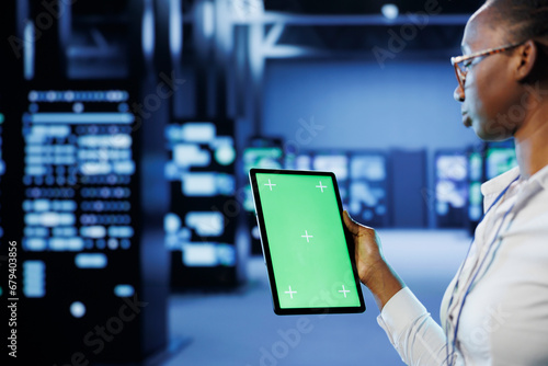 Technician in server room using green screen tablet to future proof network from downtimes and unexpected system failures. Expert with chrome key device ensuring increased data security
