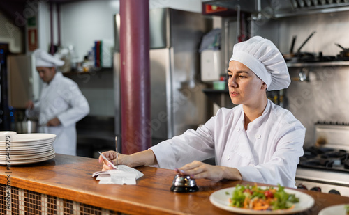 Female cook reads the paid check and presses the bell for the waiter in the restaurant