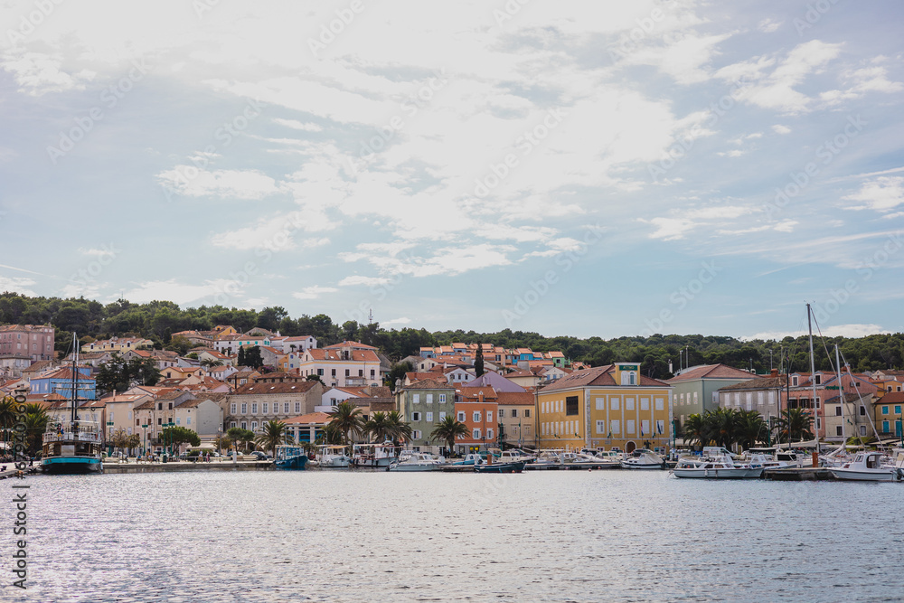 View of houses rising above the mali losinj bay across the marina, on a sunny autumn day. Different boats in the foreground.