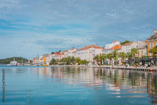 Promenade with palms and other trees and houses in the background in the city of Mali Losinj, on croatian island of Losinj, on a sunny day in autumn. Almost no people visible.