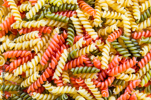 Closeup of three color fusilli variety pasta in beautiful colorful texture. Culinary background from many raw dried rotini yellow and red or green colored with tomato or spinach flavor. Italy cuisine.