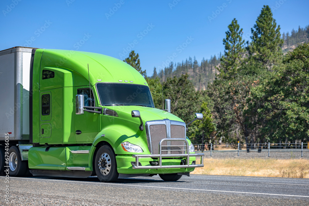 Bonnet green big rig semi truck tractor transporting commercial cargo in dry van semi trailer driving on the one way mountain highway road Bonnet green big rig semi truck tractor transporting commercial cargo in dry van semi trailer driving on the one way mountain highway road