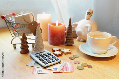 Saving money on holiday shopping, calculator, piggy bank, coins and banknotes on a table among Christmas decoration, candles and a shopping cart, copy space, selected focus photo