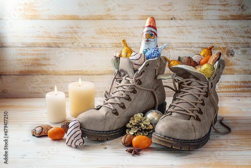 Winter boots, sweets, Christmas decoration and a chocolate Santa against rustic wood, tradition on Nicholas day or in German Nikolaus Tag to fill shoes at 6th December, copy space photo