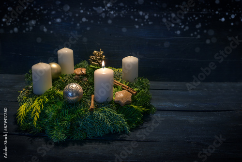 Green advent wreath with white candles, one is lit for first advent, Christmas decoration and cookies, dark blue wooden background with star bokeh, copy space