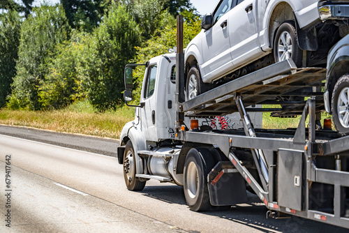 Compact day cab big rig car hauler semi truck transporting crossovers on hydraulic semi trailer driving on the highway road