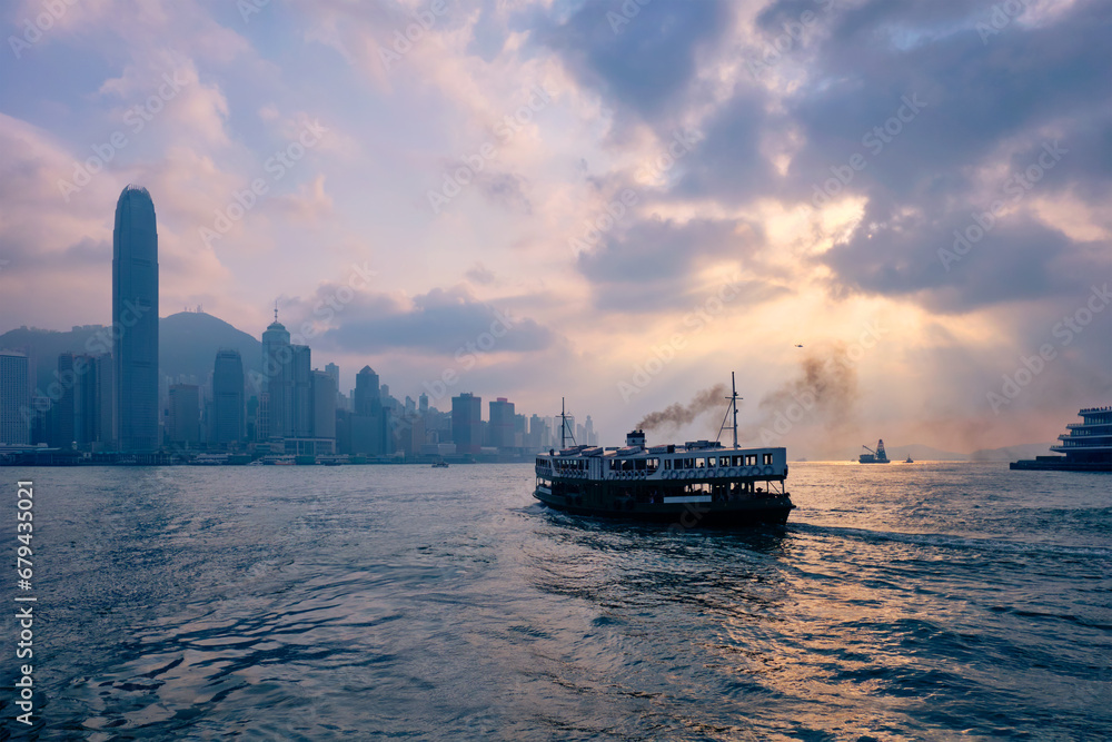 Fototapeta premium Hong Kong skyline cityscape downtown skyscrapers over Victoria Harbour on sunset with tourist ferry boat silhouette. Hong Kong, China
