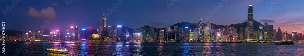 Panorama of Hong Kong skyline cityscape downtown skyscrapers over Victoria Harbour in the evening illuminated tourist boats and ferries . Hong Kong, China - obrazy, fototapety, plakaty 