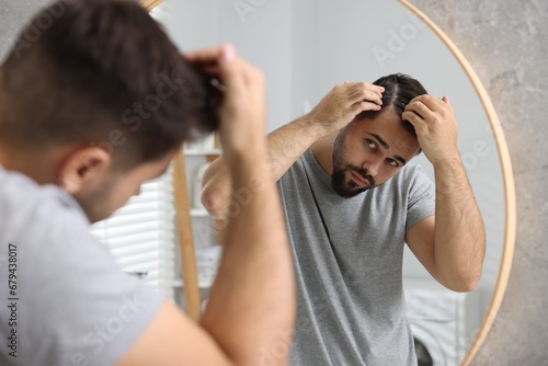 Man with dandruff in his dark hair near mirror in bathroom