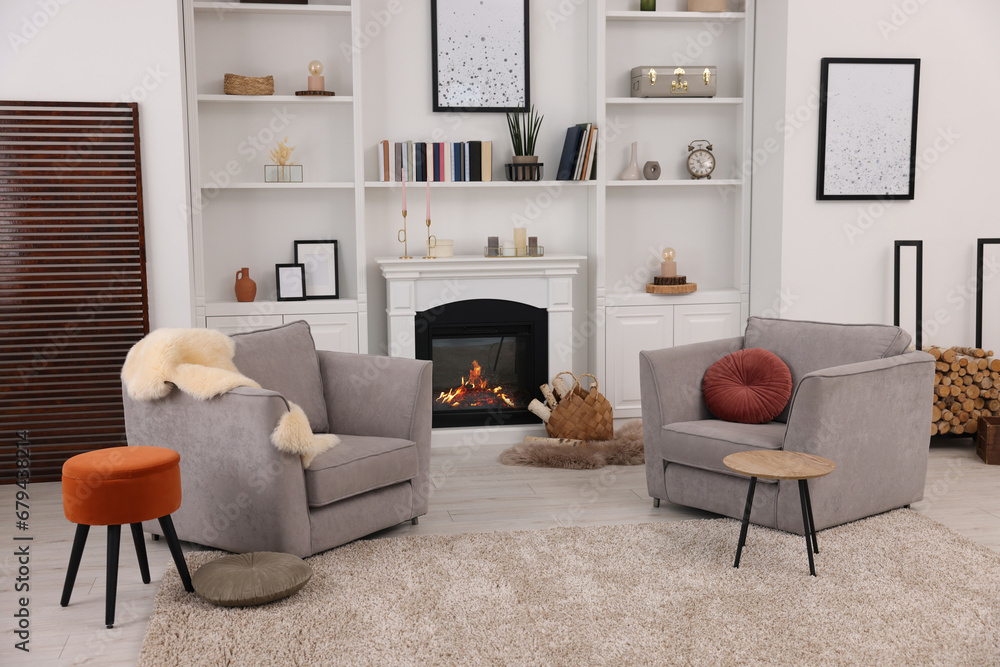 Fototapeta premium Comfortable armchairs, fireplace and shelves in living room. Interior design