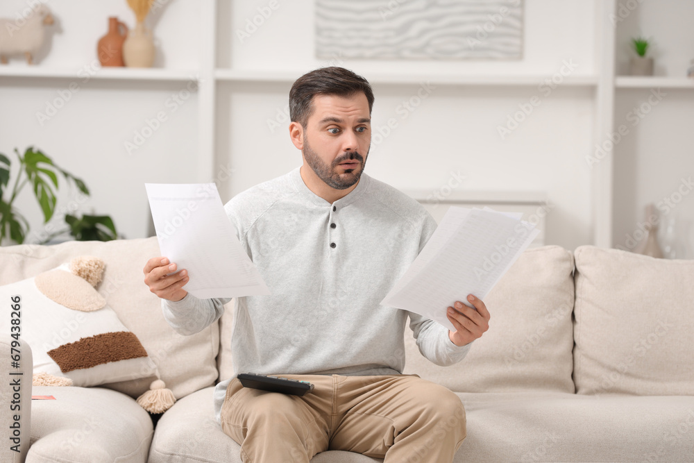 Shocked man with debt notifications and calculator planning budget at home. Financial problem Shocked man with debt notifications and calculator planning budget at home. Financial problem