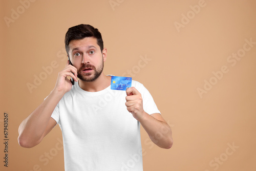 Shocked man with credit card talking on smartphone against beige background, space for text. Be careful - fraud